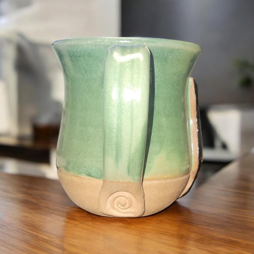 Green and beige ceramic mug on a wooden surface with a blurred background