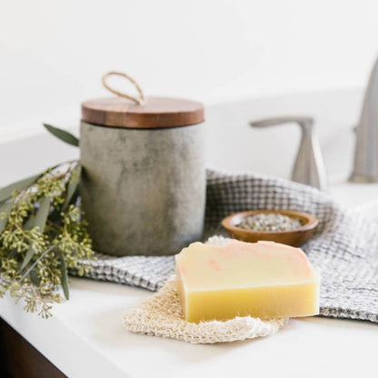 Bar of soap on a washcloth with a jar and towel in the background