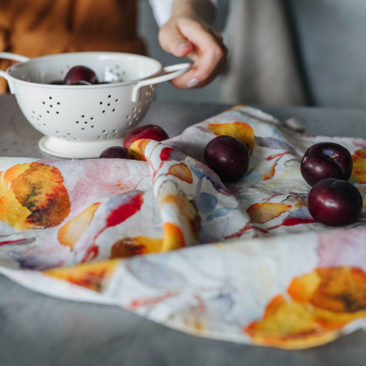 Plums on a colorful tea towel with a colander in the background