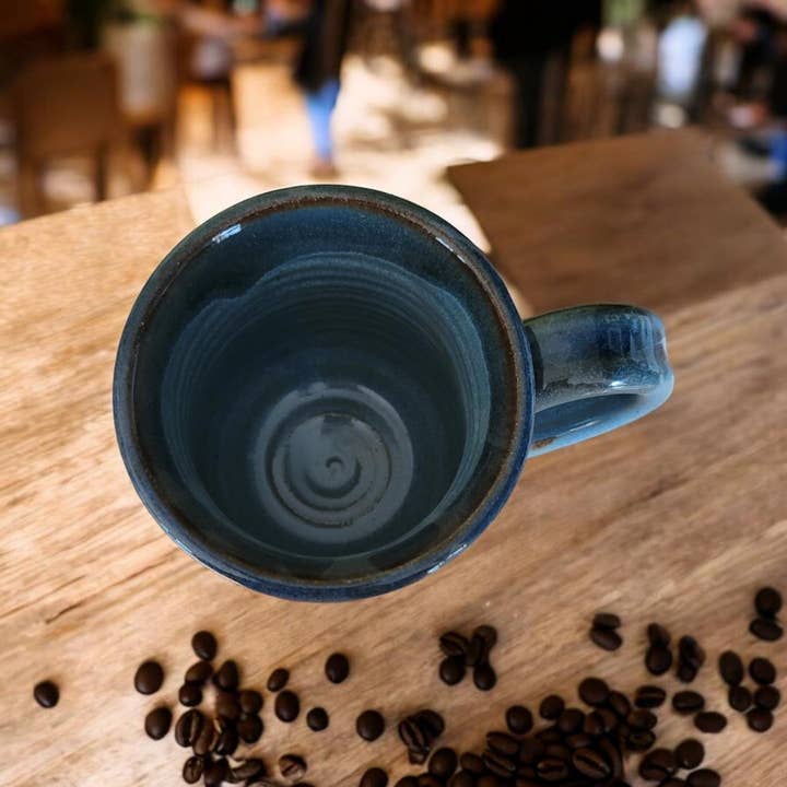 Blue ceramic mug on a wooden surface with scattered coffee beans