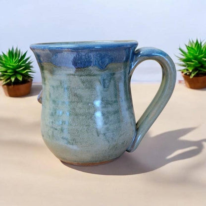 Blue and green ceramic mug on a light surface with plants in the background