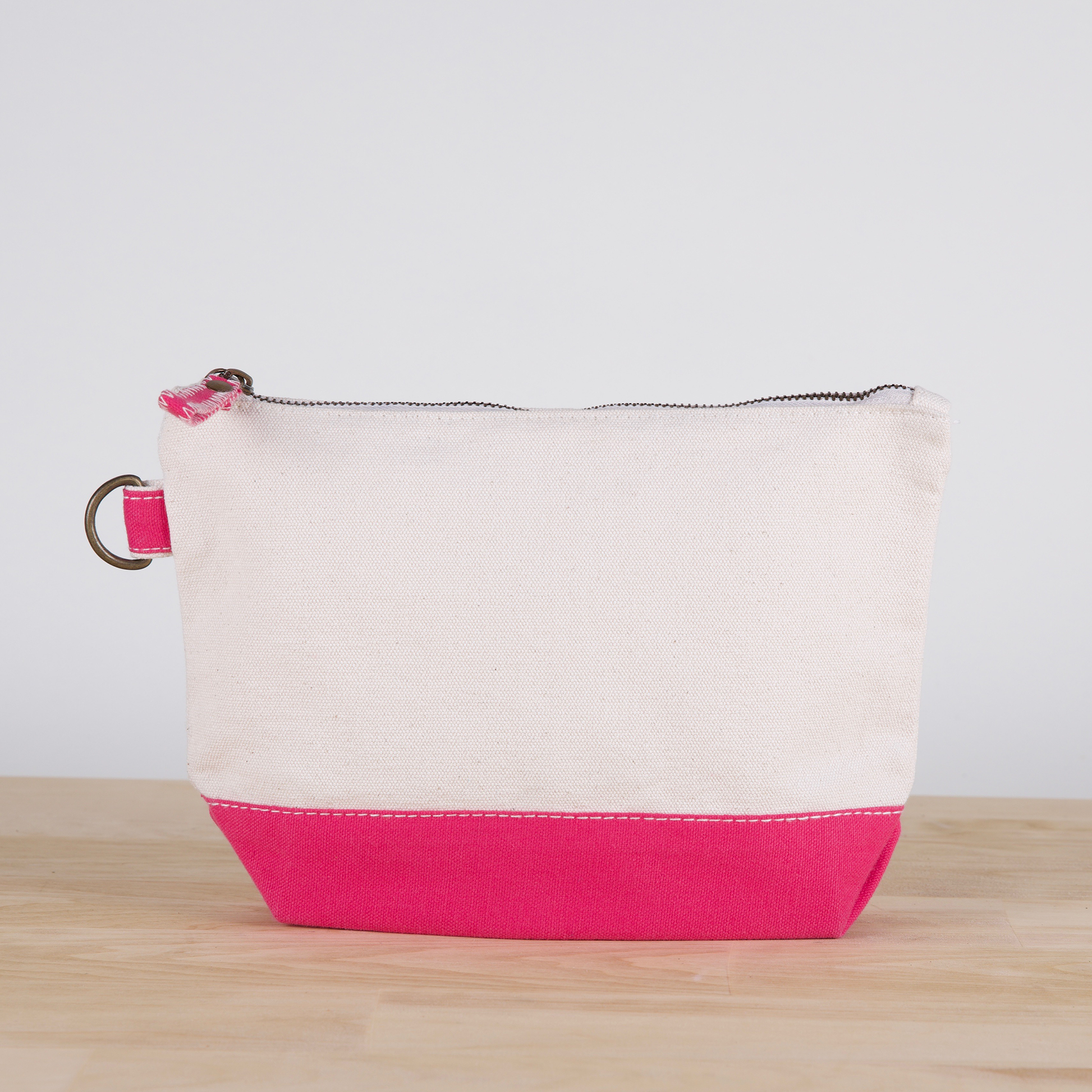 White and pink pouch on a wooden surface with a light gray background