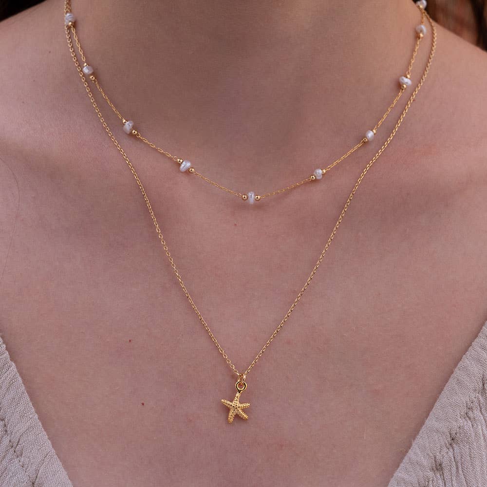 Gold necklace with a starfish pendant worn by a person