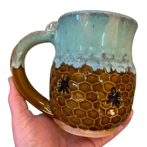 Hand holding a ceramic mug with honeycomb design and bee decorations on a white background