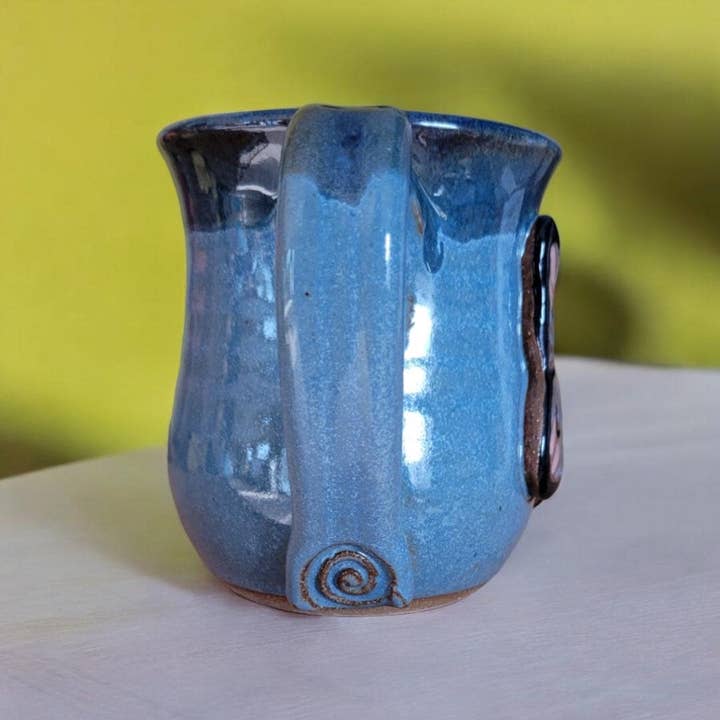 Blue ceramic mug with a handle on a white surface with a yellow background