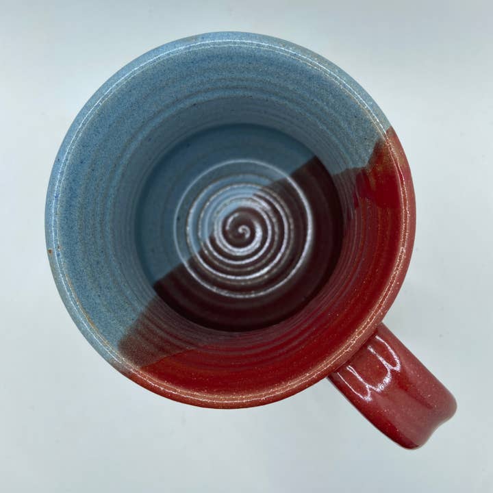 Ceramic mug with half red, half blue glaze on a light gray background