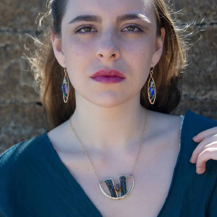 Woman wearing a necklace and earrings against a stone wall background