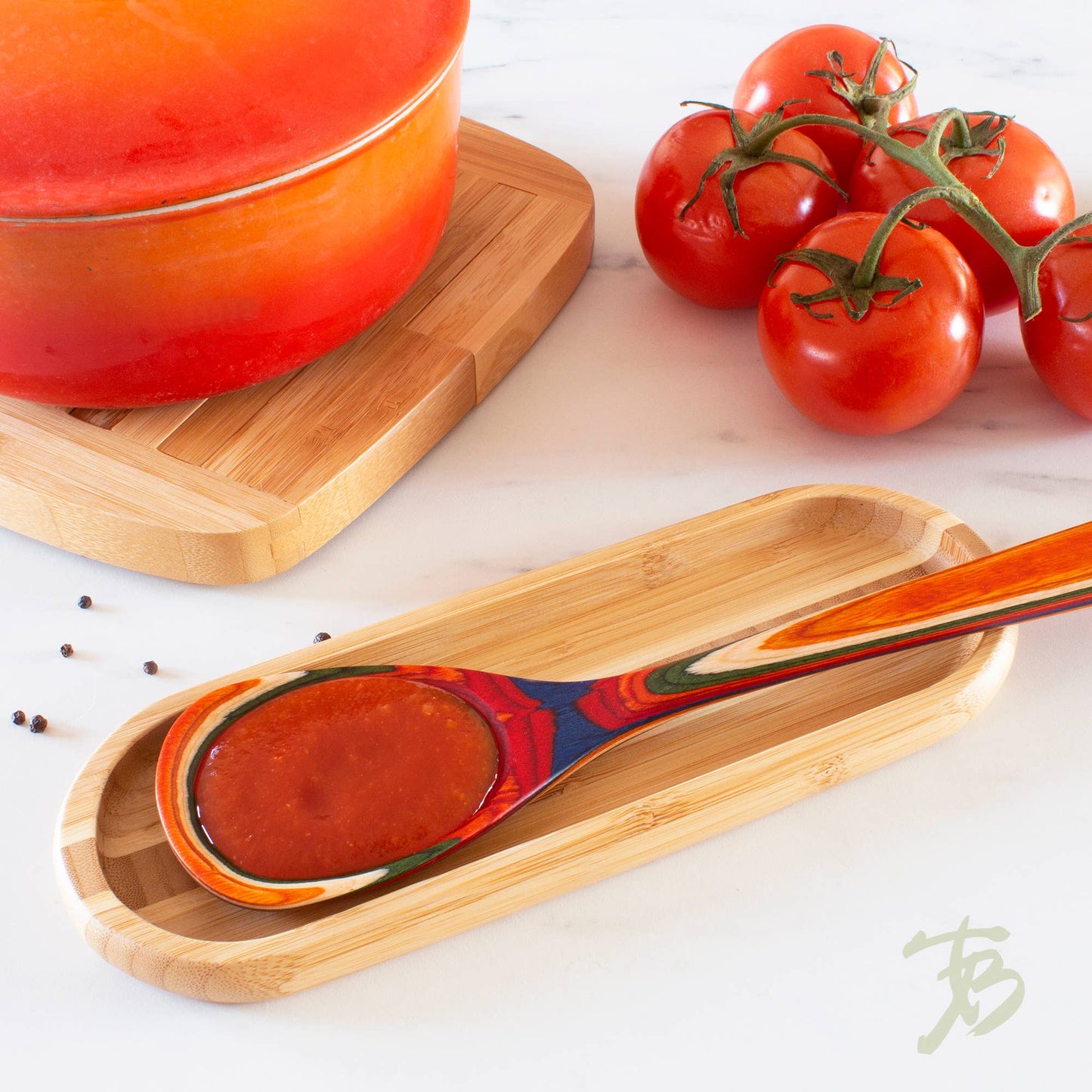 Wooden spoon with red sauce on a wooden tray, surrounded by tomatoes and a pot.