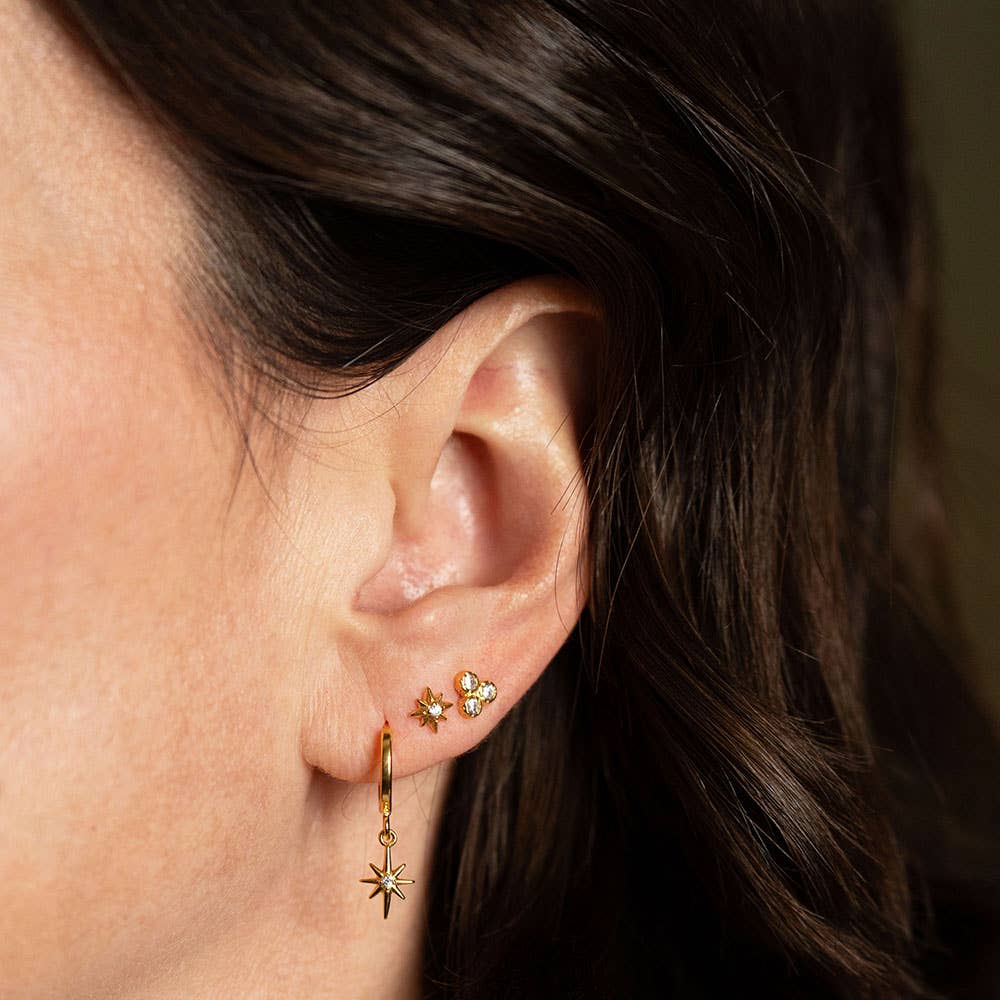 Close-up of an ear wearing gold hoop earrings with star designs.