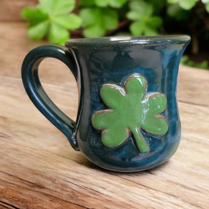 Blue mug with a green four-leaf clover design on a wooden surface