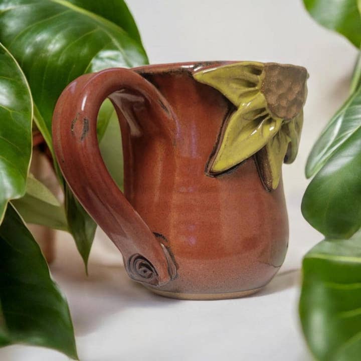 Ceramic mug with sunflower design surrounded by green leaves