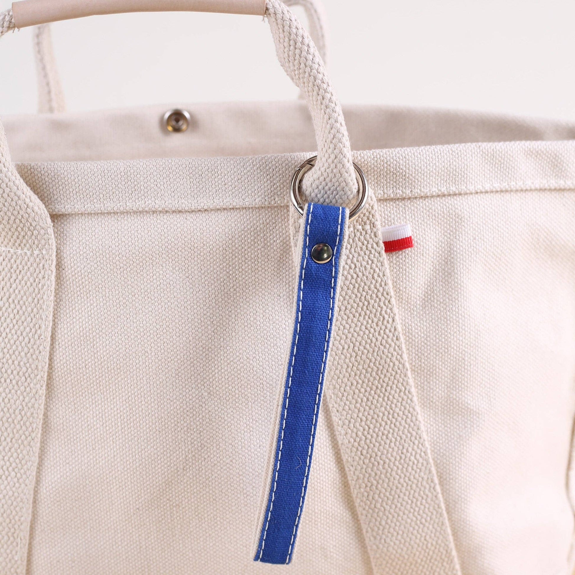 Close-up of a beige tote bag with a blue strap and red tag.