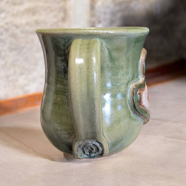 Green ceramic mug with a unique handle design on a neutral background