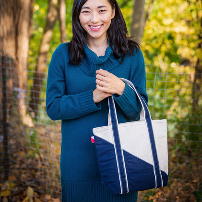 Woman holding a blue and white tote bag outdoors with greenery in the background