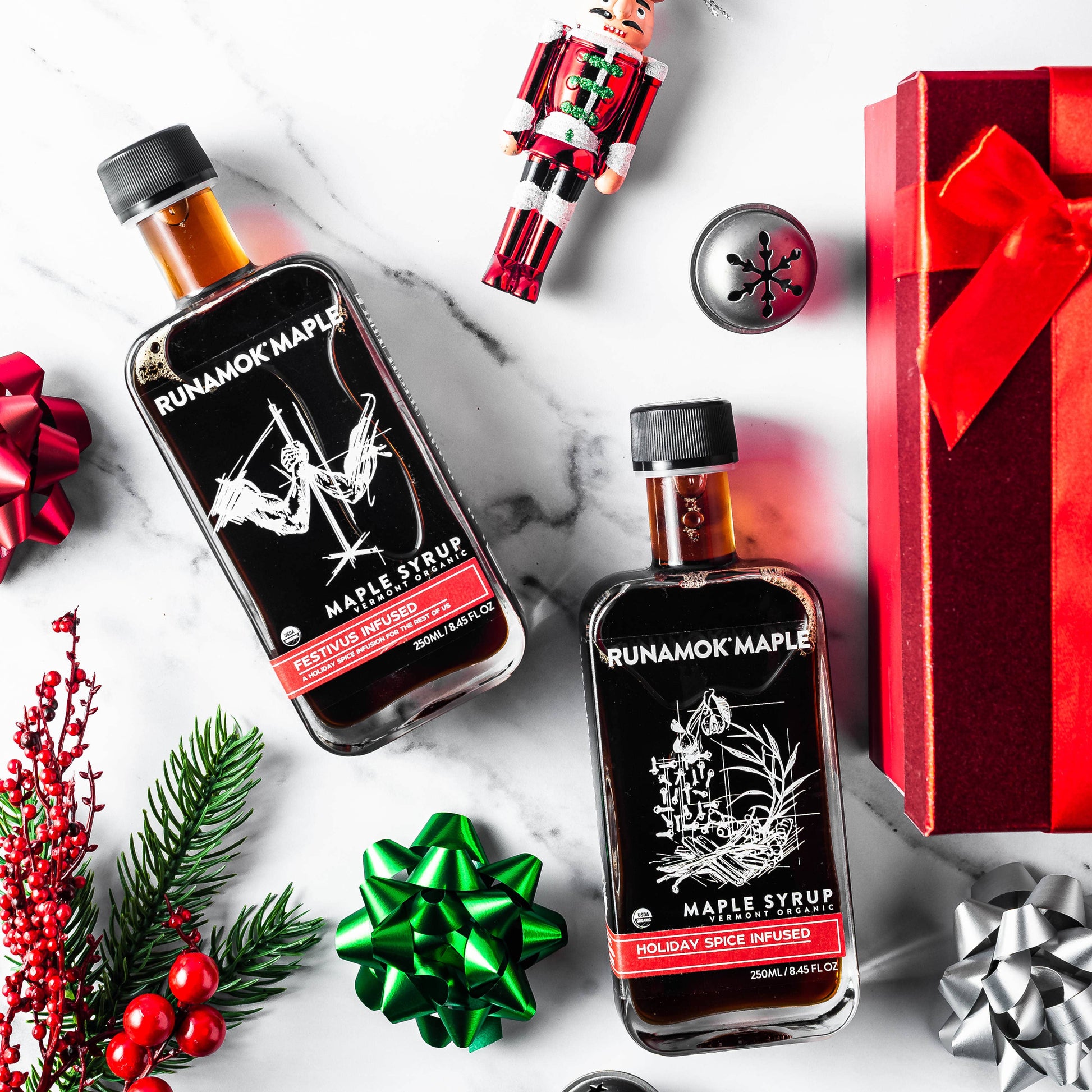 Two bottles of Runamok Maple syrup with holiday decorations on a white marble surface.