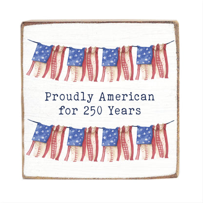 Decorative sign with American flags and text 'Proudly American for 250 Years' on a white background.