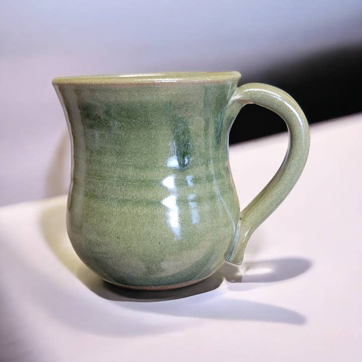 Green ceramic mug on a white surface with a gray background