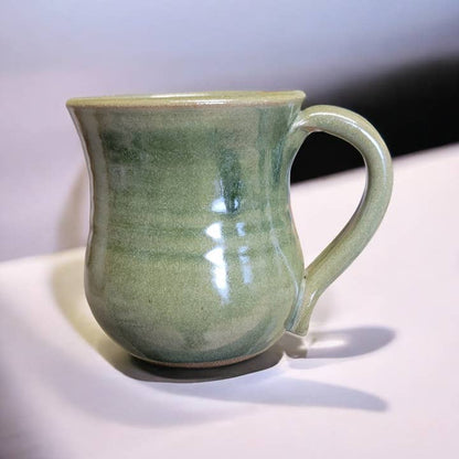 Green ceramic mug on a white surface with a gray background