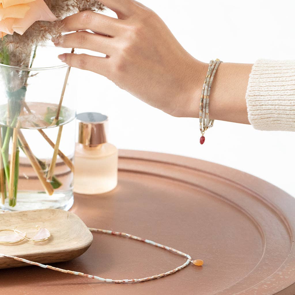 Hand with bracelet near a vase, necklace, and flowers on a wooden surface