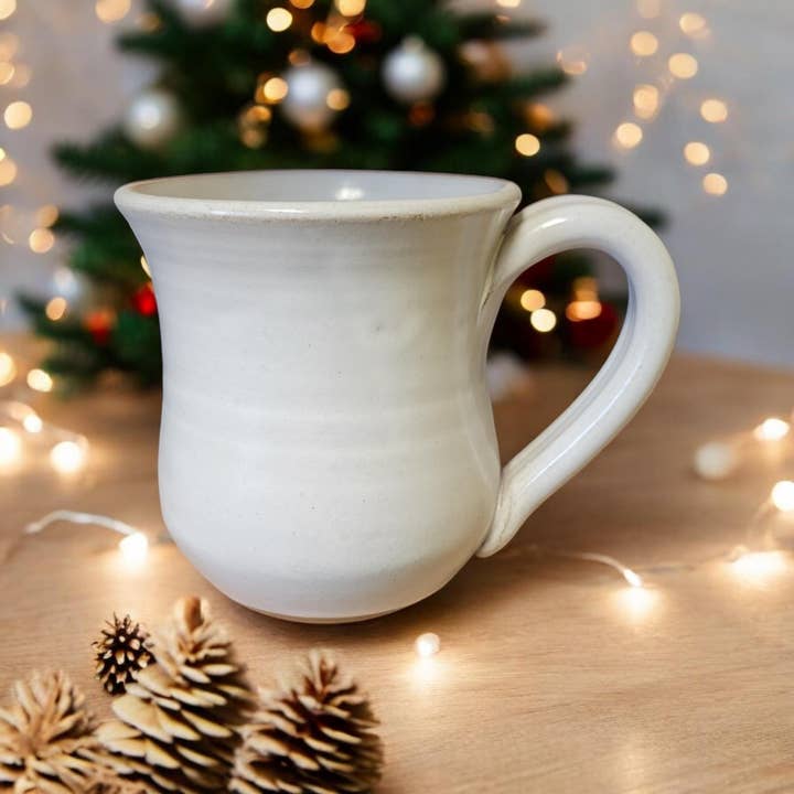 White mug on a wooden surface with Christmas decorations and lights in the background