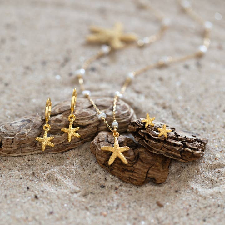 Gold starfish earrings on a sandy surface with driftwood
