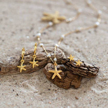 Gold starfish earrings on a sandy surface with driftwood