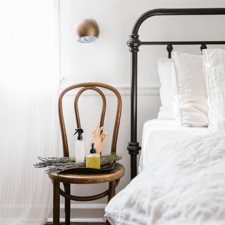 Bedroom with a wooden chair holding a bottle and a lavender bunch, next to a bed with white bedding.