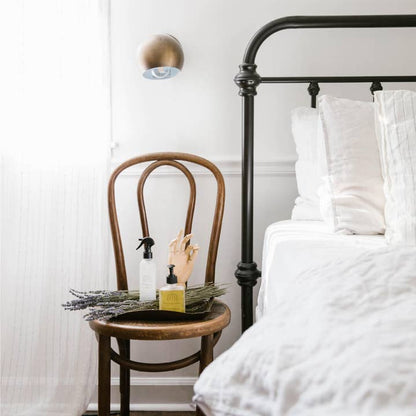 Bedroom with a wooden chair holding a bottle and a lavender bunch, next to a bed with white bedding.