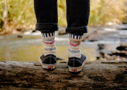 Person wearing patterned socks and dark shoes standing on a log with a natural background