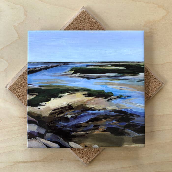Square trivet with a coastal landscape design on a wooden surface