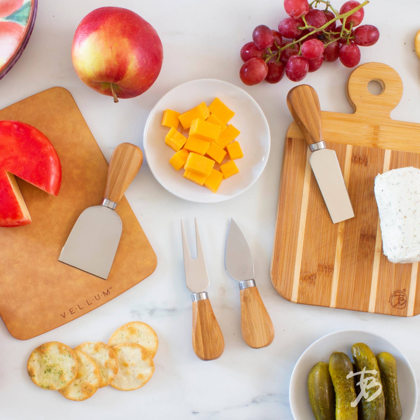 Wooden cutting boards with cheese knives, fruits, and snacks on a marble surface