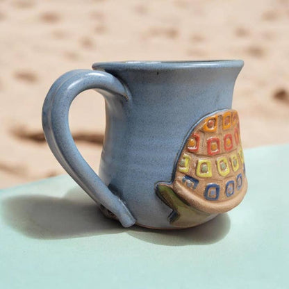 Ceramic mug with a colorful geometric turtle design on a light surface