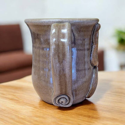 Ceramic mug with a unique handle design on a wooden table.