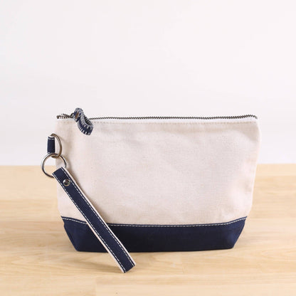 White pouch with navy accents and a matching strap on a light wooden surface.