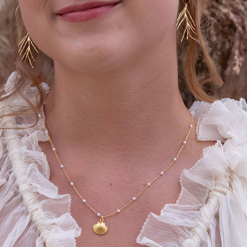 Close-up of a woman wearing a gold necklace with a shell pendant and gold earrings.