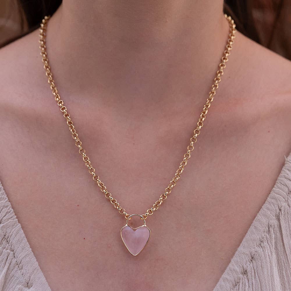 Gold chain necklace with a pink heart pendant on a person wearing a light-colored top.