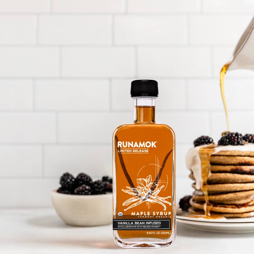 Bottle of Runamok maple syrup with pancakes and blackberries on a kitchen counter.