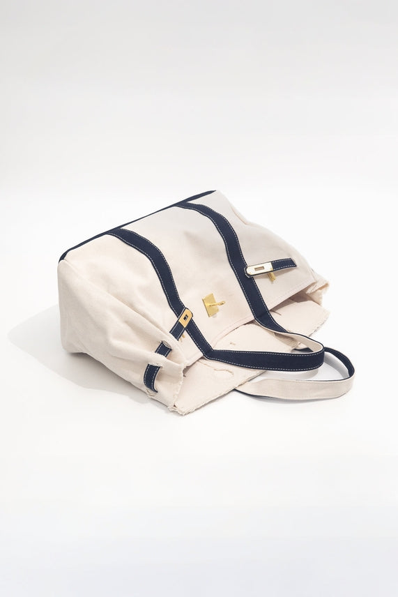 Beige handbag with navy accents leaning on its side on a white background