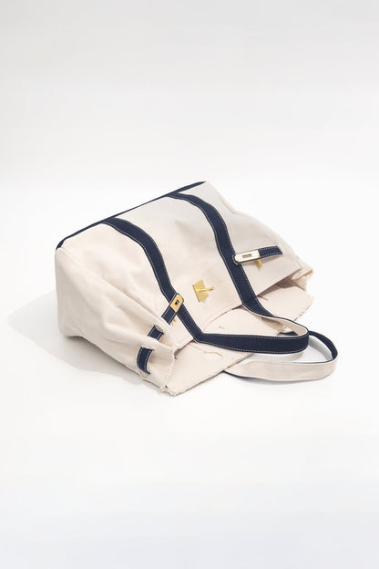 Beige handbag with navy accents leaning on its side on a white background