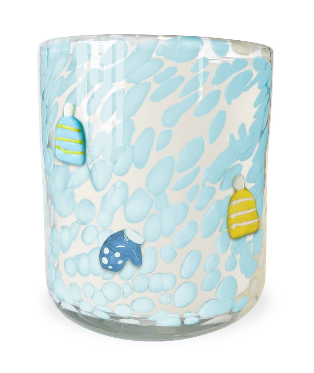 Glass candle with blue and white pattern and hat and mitten decorations on a white background.