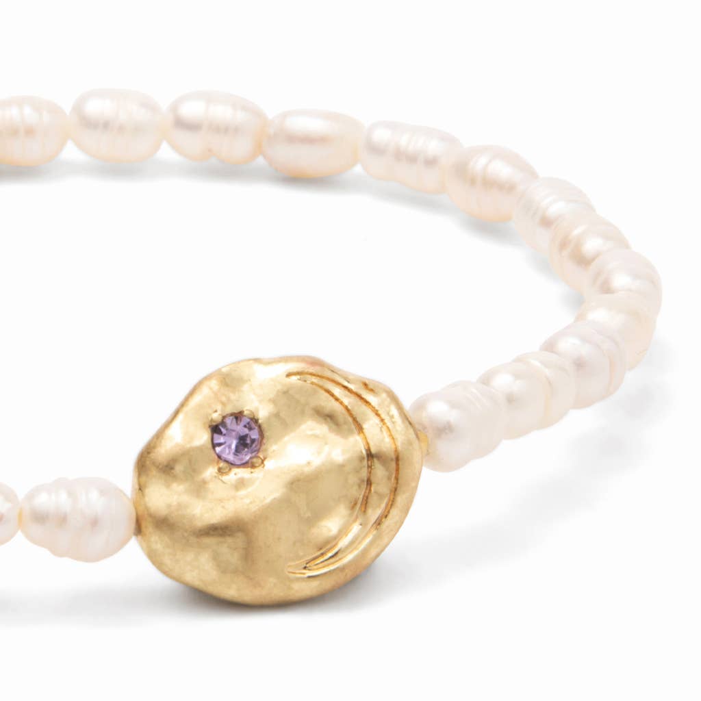 Detail of a pearl bracelet with gold disc with purple gemstone on a white background.