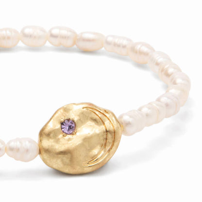 Detail of a pearl bracelet with gold disc with purple gemstone on a white background.