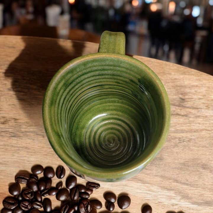 Green ceramic mug on a wooden table with coffee beans