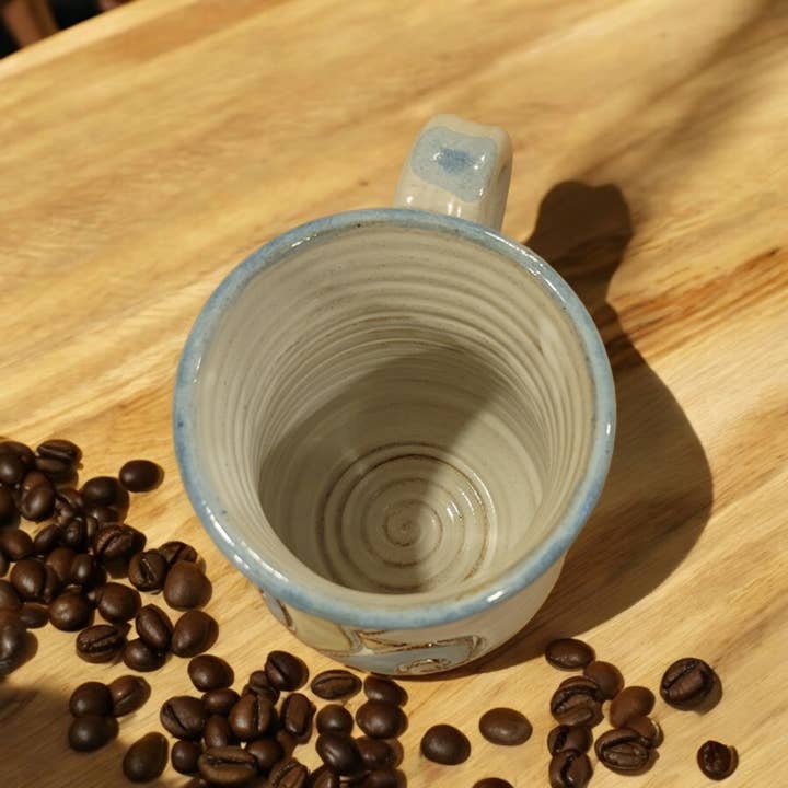 Empty ceramic mug on a wooden surface with scattered coffee beans