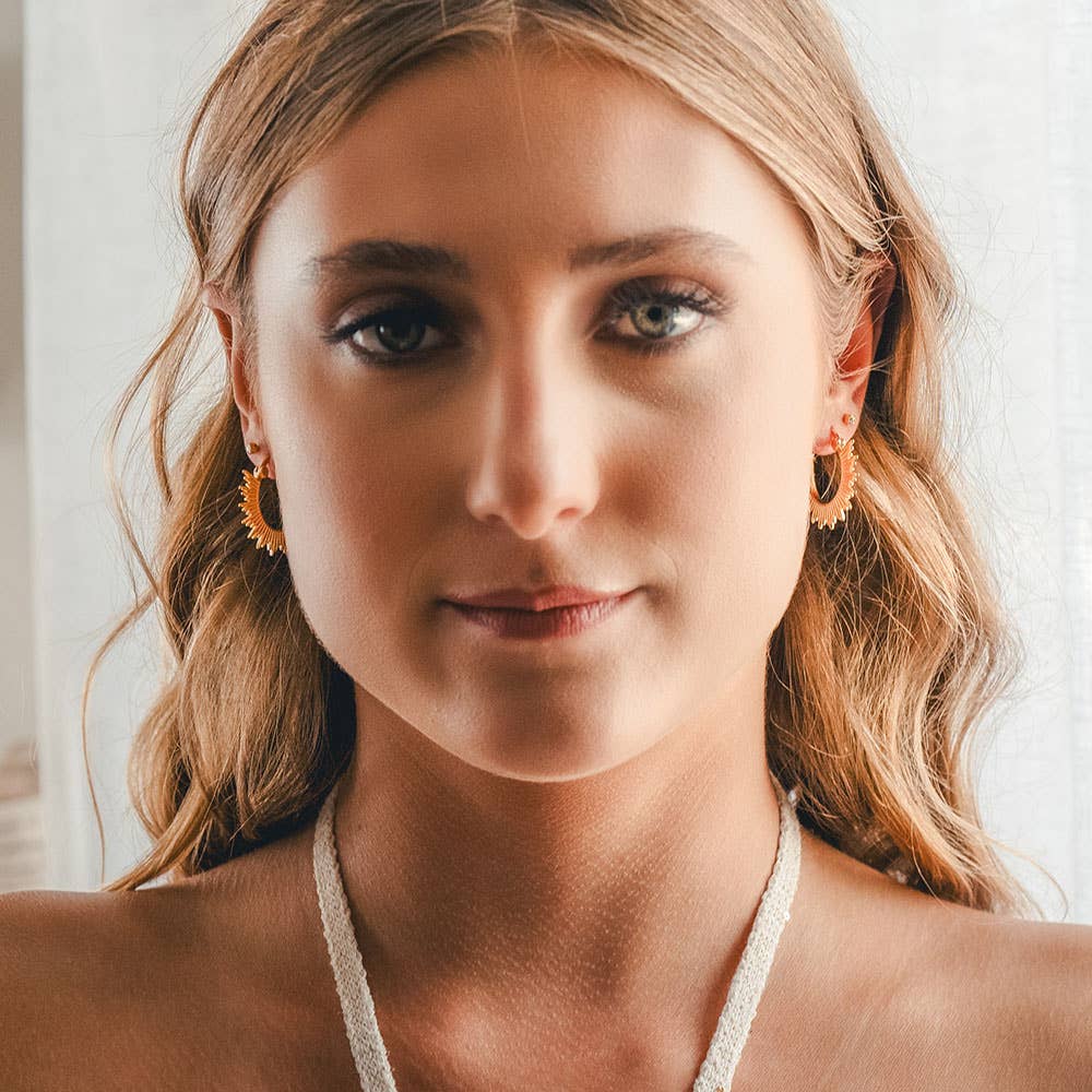Woman wearing a white halter top and gold earrings with a blurred background