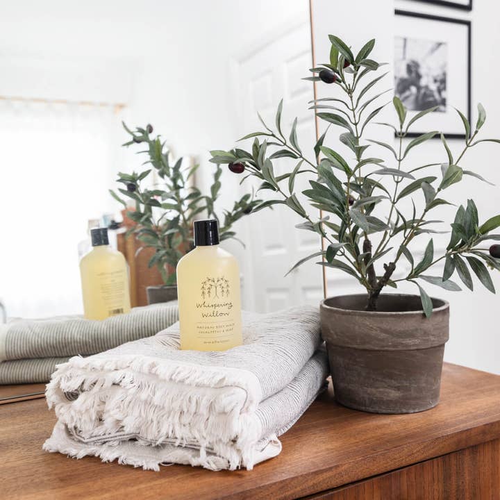 Bottle of body wash on a towel with a potted plant on a wooden surface
