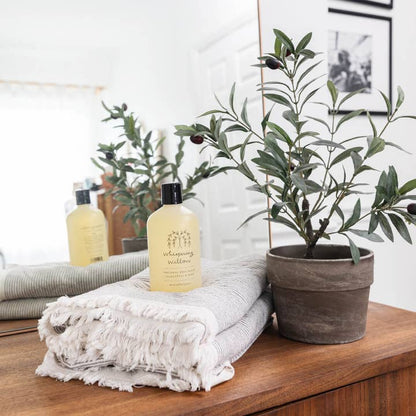 Bottle of body wash on a towel with a potted plant on a wooden surface