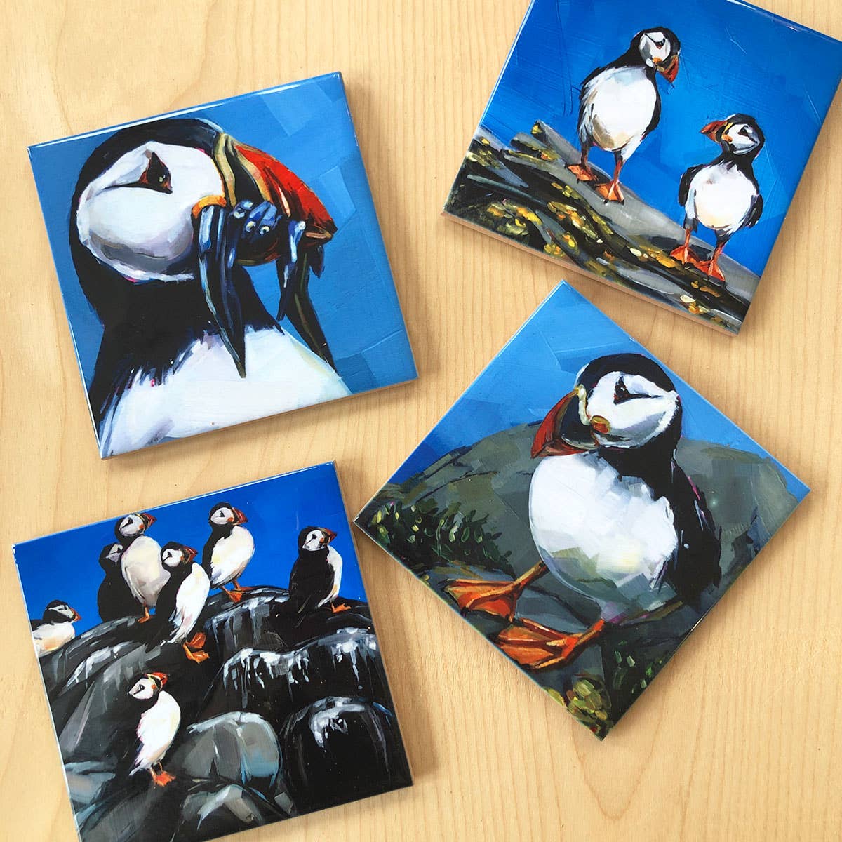 Four square coasters with puffin illustrations on a wooden surface