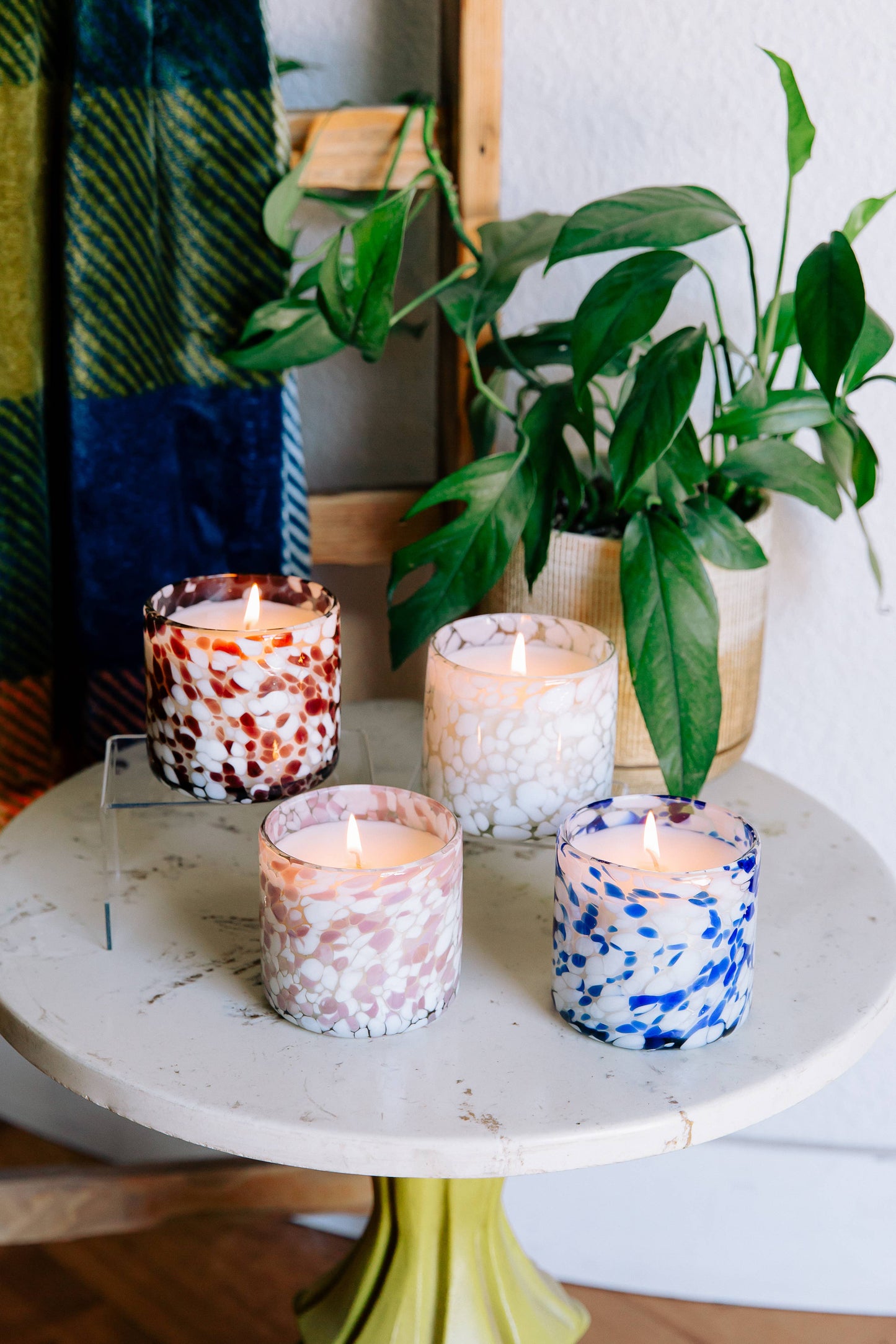 Four colorful candles on a round stone surface with plants in the background