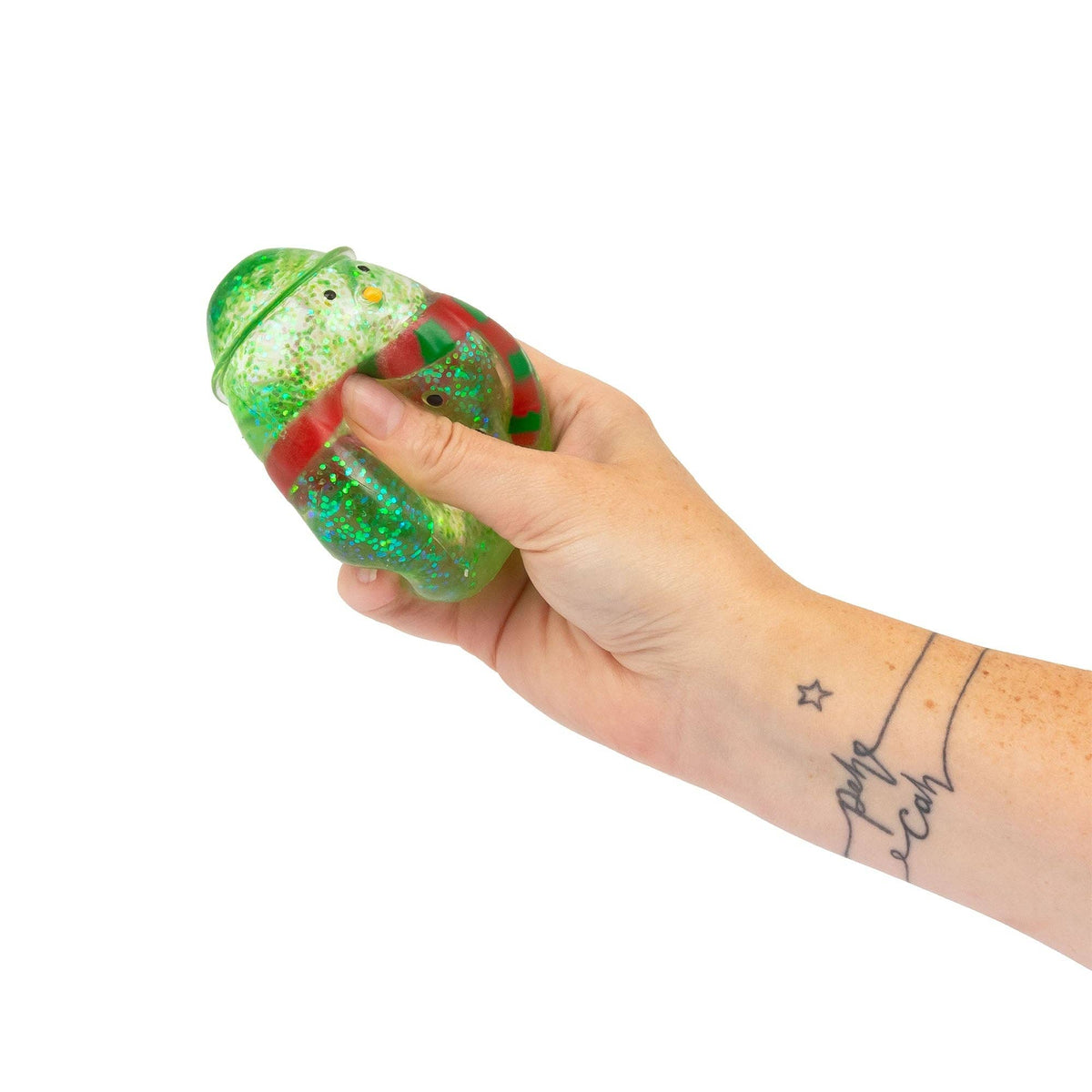 A hand holding a green glittery snowman shaped squishy toy with red accents, shown against a plain white background.